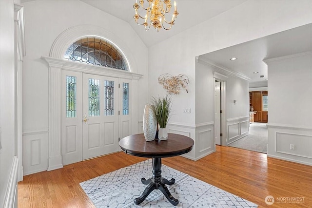 entryway with light wood-type flooring, a wainscoted wall, a decorative wall, a chandelier, and vaulted ceiling