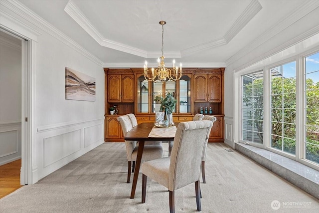 dining area featuring a chandelier, light colored carpet, a tray ceiling, wainscoting, and a decorative wall