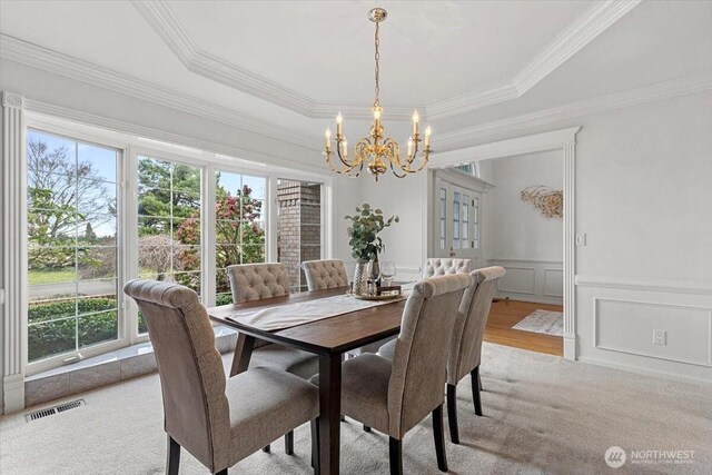 dining area with an inviting chandelier, a raised ceiling, a decorative wall, and visible vents