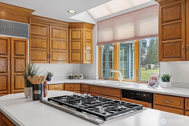 kitchen with dishwashing machine, brown cabinetry, stainless steel gas cooktop, a sink, and light countertops