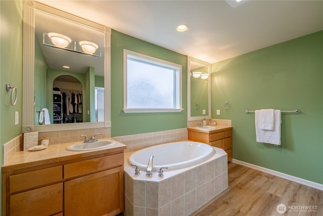 bathroom with wood finished floors, two vanities, a garden tub, and a sink