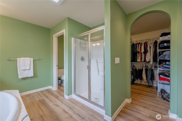 full bath featuring a walk in closet, toilet, wood finished floors, and a stall shower