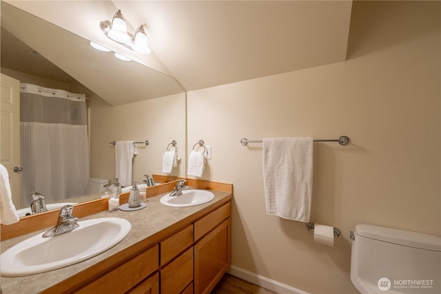 full bathroom featuring double vanity, vaulted ceiling, toilet, and a sink