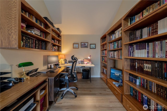 office area with vaulted ceiling, light wood-style flooring, wall of books, and baseboards