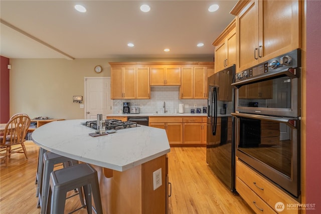 kitchen featuring light wood finished floors, a sink, decorative backsplash, black appliances, and a center island