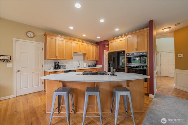 kitchen with black appliances, a kitchen island, arched walkways, light wood finished floors, and light countertops