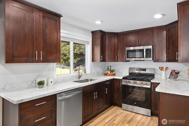 kitchen with light stone counters, recessed lighting, light wood-style flooring, appliances with stainless steel finishes, and a sink