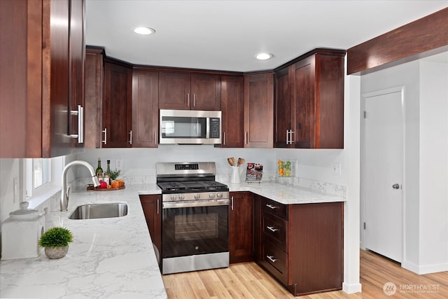 kitchen featuring light stone counters, light wood-type flooring, appliances with stainless steel finishes, and a sink