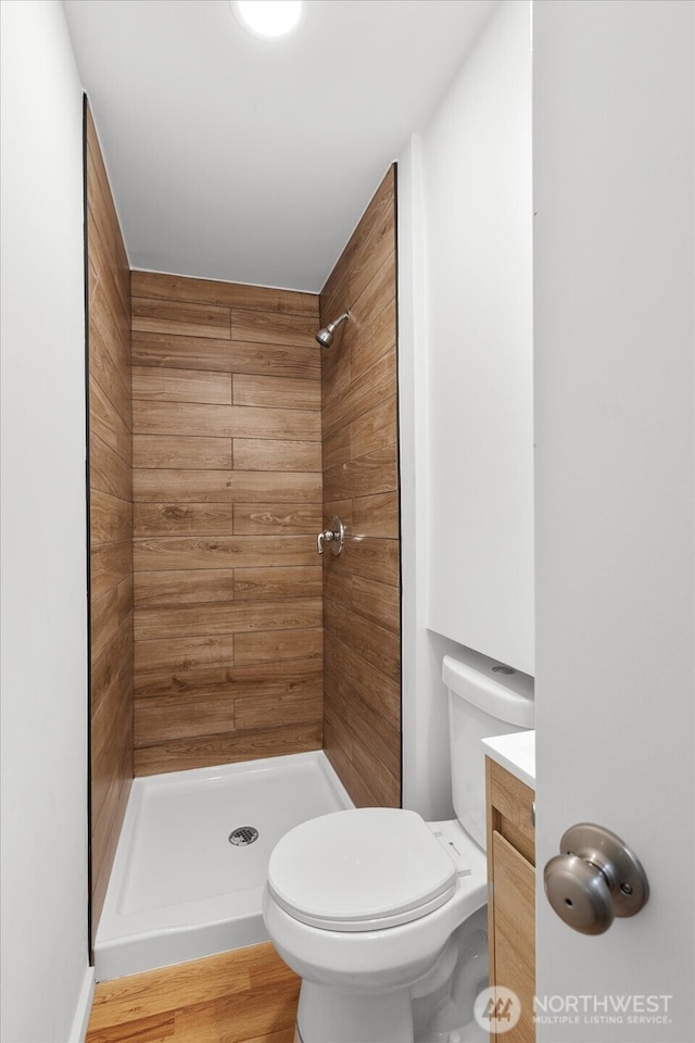 full bath with vanity, toilet, wood finished floors, and a tile shower