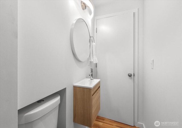 half bath with toilet, wood finished floors, and vanity
