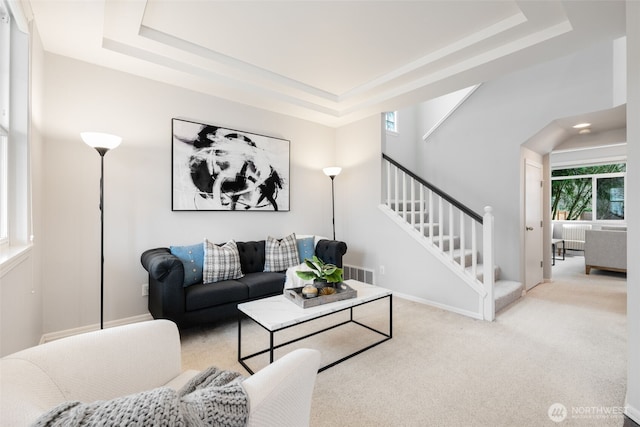 carpeted living room with stairs, a raised ceiling, baseboards, and visible vents