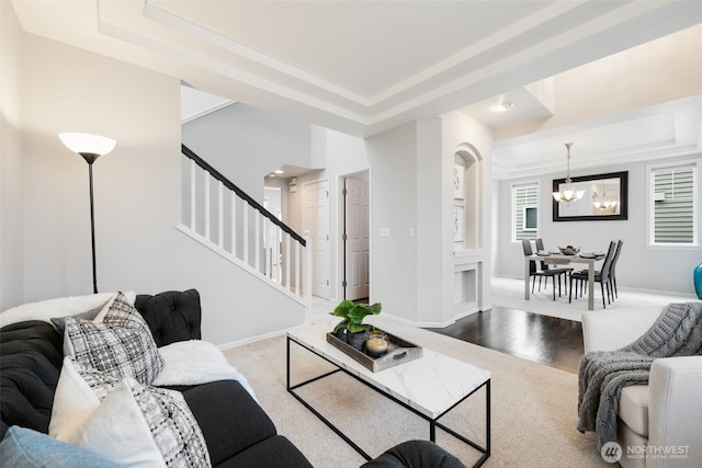 living area with an inviting chandelier, a raised ceiling, stairway, and baseboards