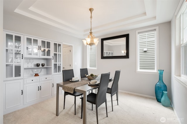 dining space featuring baseboards, a raised ceiling, and light carpet