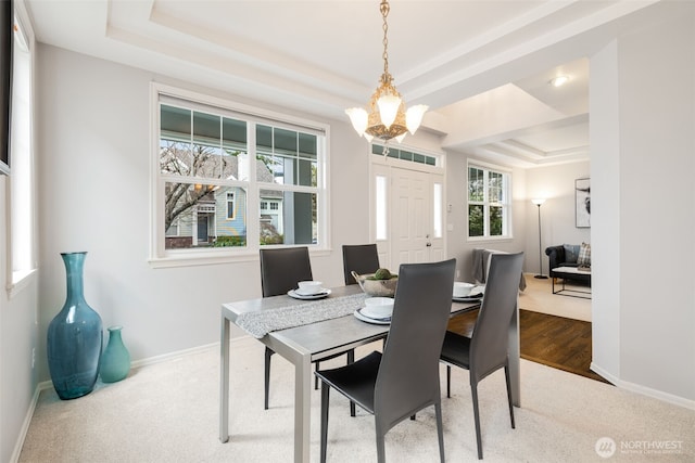 dining space featuring a notable chandelier, carpet flooring, baseboards, and a tray ceiling