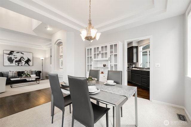 carpeted dining area featuring a raised ceiling, baseboards, a chandelier, and a sink