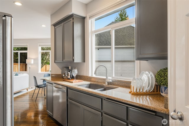 kitchen with light stone counters, dark wood-style floors, gray cabinets, a sink, and stainless steel appliances