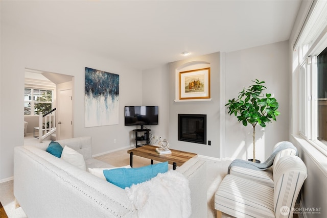 living room with baseboards, carpet floors, a glass covered fireplace, and stairs