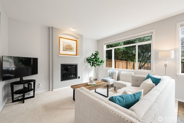 carpeted living room with a glass covered fireplace and baseboards