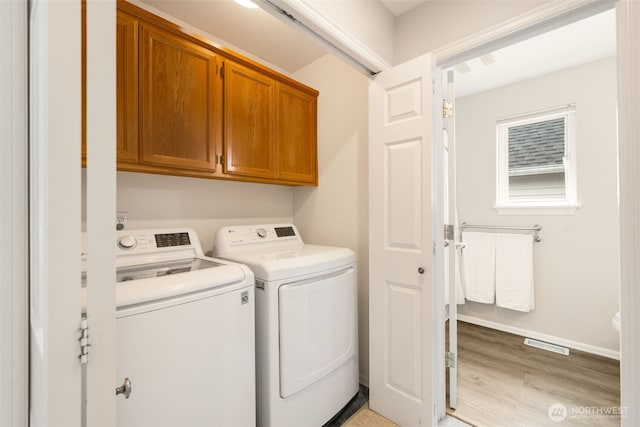 clothes washing area featuring visible vents, baseboards, washing machine and dryer, light wood-style floors, and cabinet space