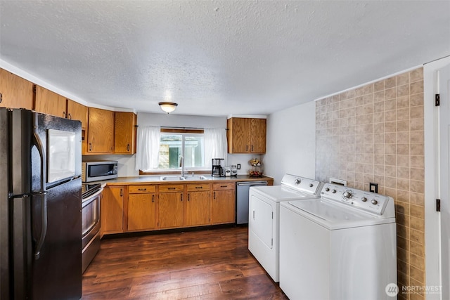 kitchen featuring brown cabinetry, washing machine and clothes dryer, dark wood finished floors, a sink, and stainless steel appliances