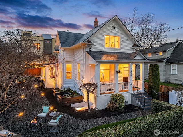 view of front of home featuring a porch, a vegetable garden, a chimney, and fence