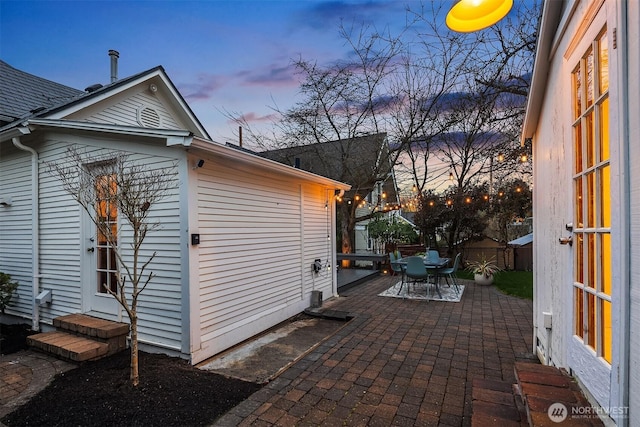 property exterior at dusk with entry steps, outdoor dining space, a patio area, and fence