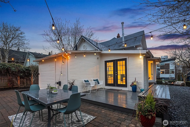 back of house at dusk with a patio area, outdoor dining area, french doors, and a wooden deck