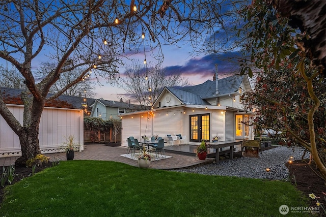 back of house at dusk with a lawn, an outbuilding, fence, french doors, and a patio area