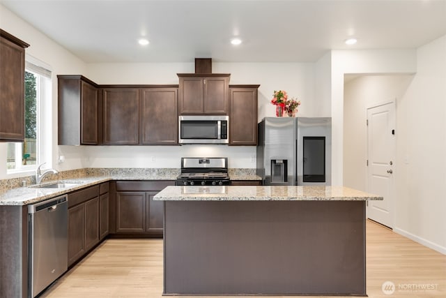 kitchen with a sink, light wood-style floors, dark brown cabinetry, and appliances with stainless steel finishes