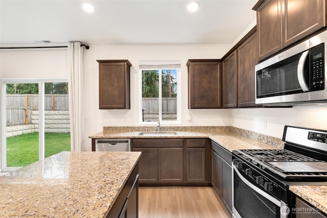 kitchen featuring light wood finished floors, dark brown cabinets, light stone counters, stainless steel appliances, and a sink