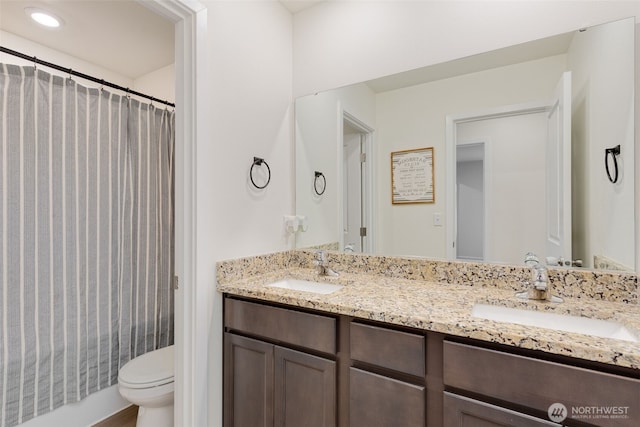 bathroom with double vanity, curtained shower, toilet, and a sink