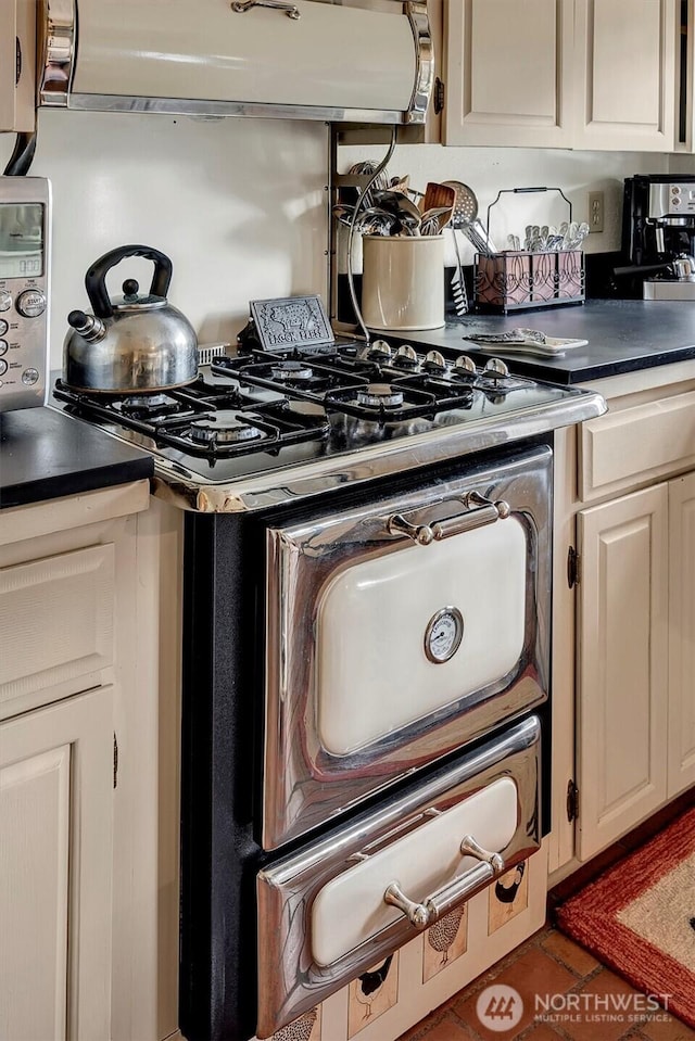 kitchen with tile patterned floors, dark countertops, range hood, white cabinetry, and gas range