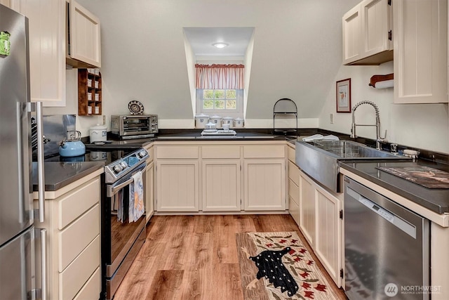 kitchen with light wood finished floors, a toaster, a sink, appliances with stainless steel finishes, and dark countertops