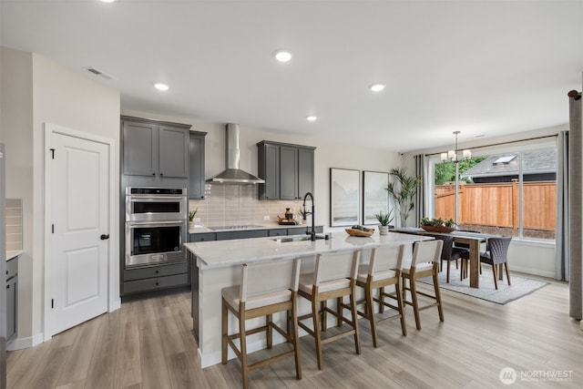 kitchen with visible vents, stainless steel double oven, a sink, wall chimney exhaust hood, and backsplash