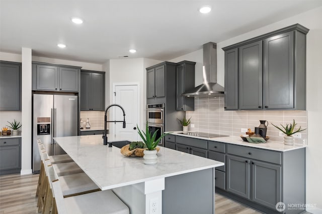 kitchen with light stone countertops, light wood finished floors, a sink, appliances with stainless steel finishes, and wall chimney exhaust hood