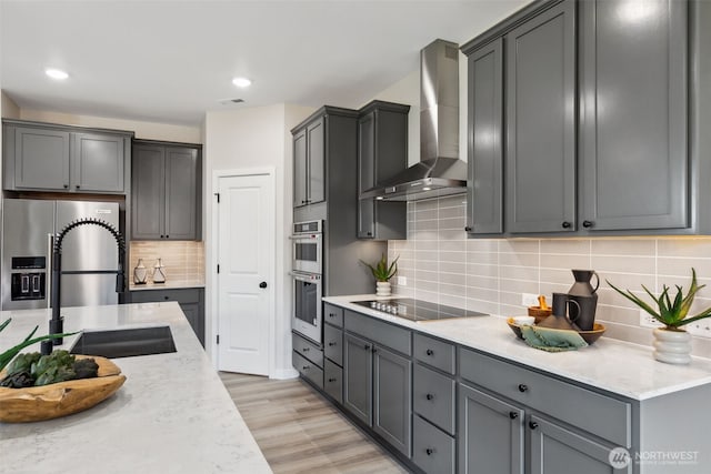 kitchen with light wood-style flooring, a sink, stainless steel appliances, wall chimney range hood, and backsplash