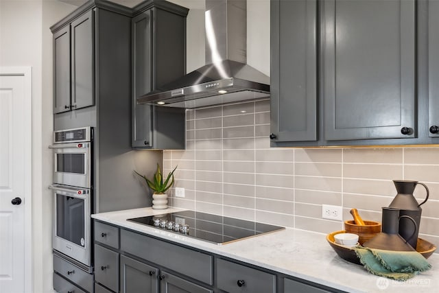 kitchen with tasteful backsplash, gray cabinetry, wall chimney range hood, stainless steel double oven, and black electric cooktop