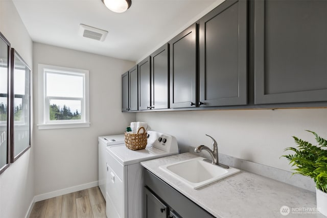 washroom with visible vents, light wood-style flooring, cabinet space, a sink, and washer and dryer