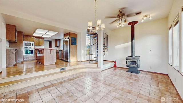 unfurnished living room featuring light tile patterned floors, plenty of natural light, stairs, and a wood stove