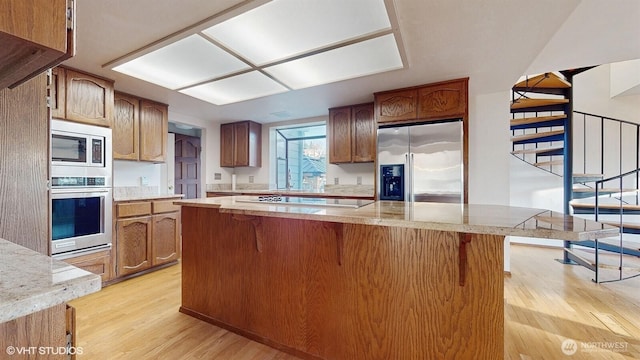 kitchen with a kitchen island, a kitchen bar, light wood-style flooring, appliances with stainless steel finishes, and brown cabinetry