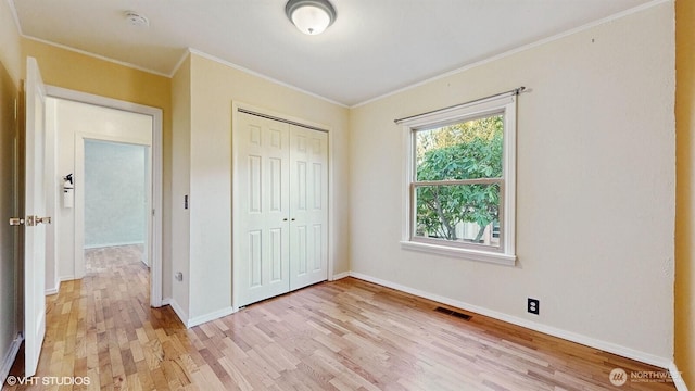 unfurnished bedroom with visible vents, baseboards, ornamental molding, light wood-style flooring, and a closet