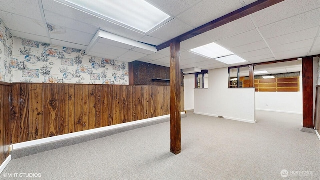 finished basement with a drop ceiling, carpet flooring, wooden walls, and wainscoting