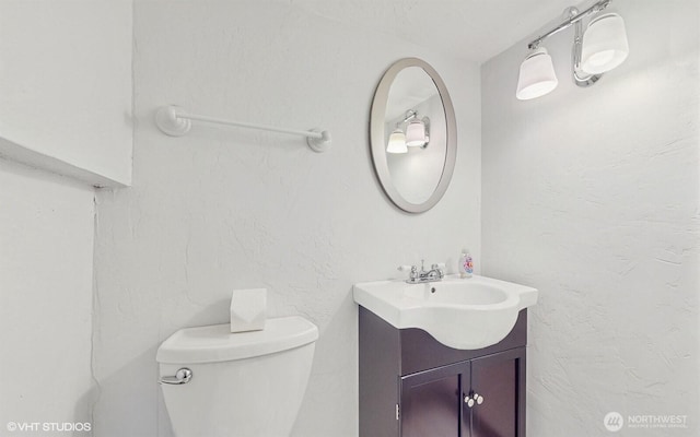 half bath with toilet, vanity, and a textured wall