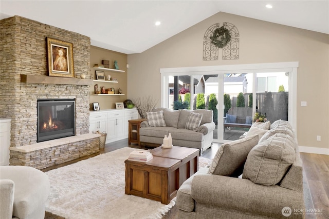 living room with baseboards, lofted ceiling, a stone fireplace, and wood finished floors