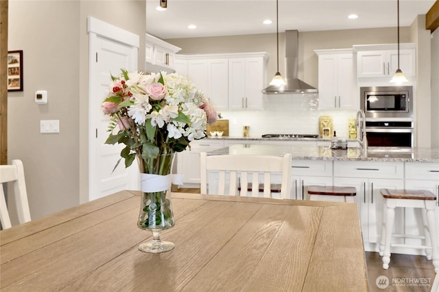 kitchen featuring stainless steel appliances, decorative backsplash, pendant lighting, white cabinetry, and wall chimney range hood