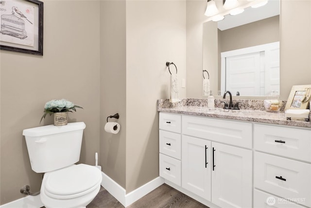 bathroom featuring baseboards, toilet, wood finished floors, and vanity