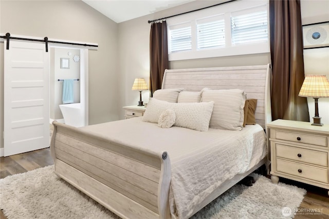 bedroom with a barn door, wood finished floors, and lofted ceiling