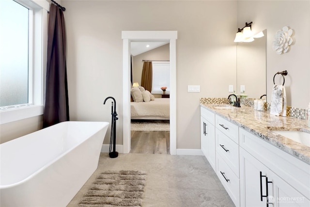 full bath with baseboards, double vanity, a freestanding tub, ensuite bath, and a sink