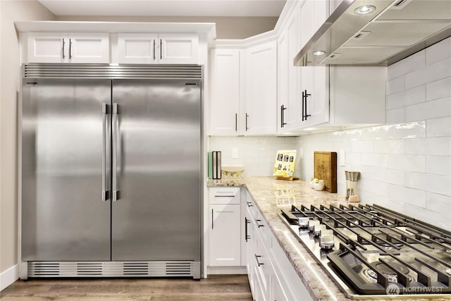 kitchen featuring light stone counters, wood finished floors, stainless steel appliances, white cabinets, and exhaust hood