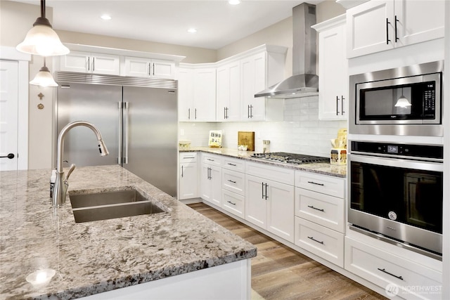 kitchen with light wood-style flooring, a sink, tasteful backsplash, wall chimney exhaust hood, and built in appliances